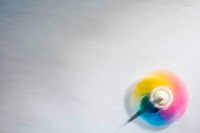 A colorful spinning top in motion creates a blur of vibrant colors against a plain white background. The motion effect adds a dynamic and playful element to the composition.