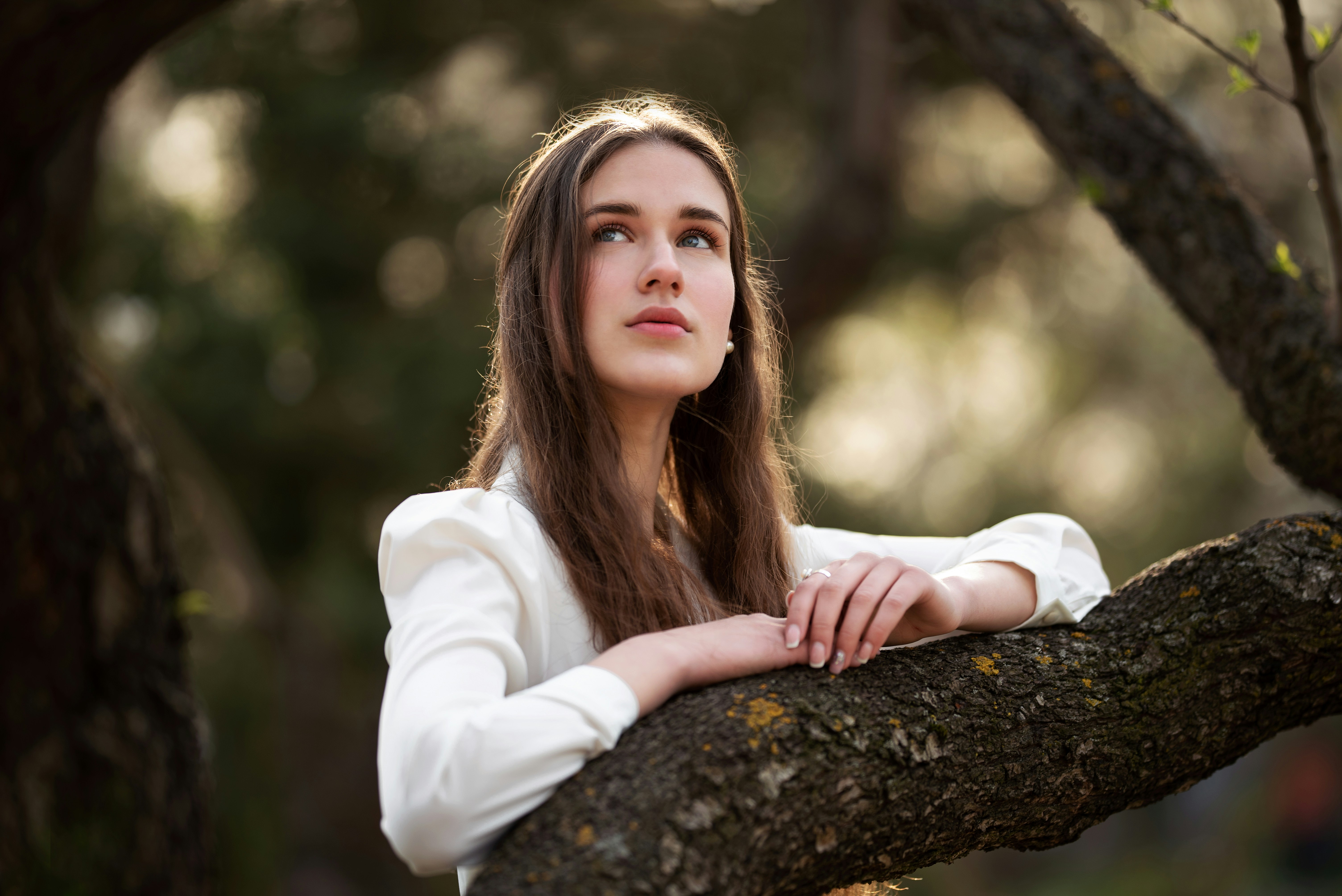 woman in white long sleeve shirt leaning on brown tree trunk