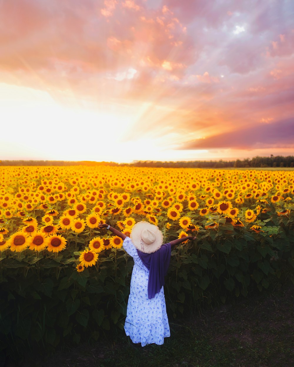 Frau in weißem Kleid steht bei Sonnenuntergang auf Sonnenblumenfeld