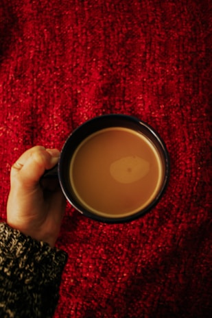 Close-up of hands holding a coffee cup, showcasing a taupe gray knitted sweater sleeve.