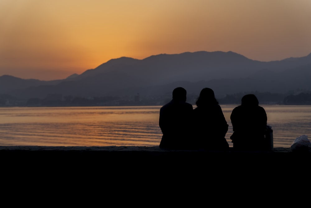 silhouette of people sitting on seashore during sunset