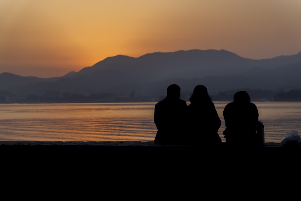 silhouette di persone sedute in riva al mare durante il tramonto