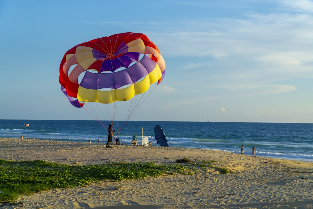 Persone sulla spiaggia con paracadute rosso, blu e giallo sotto il cielo blu durante il giorno