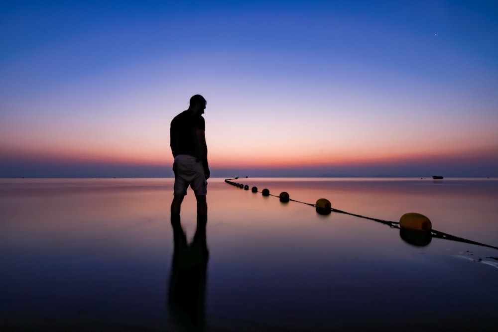 silhouette of man standing on seashore during sunset