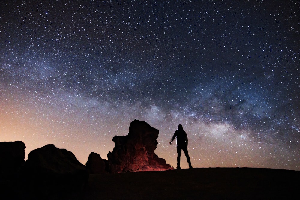 silhouette dell'uomo in piedi sulla formazione rocciosa sotto la notte stellata