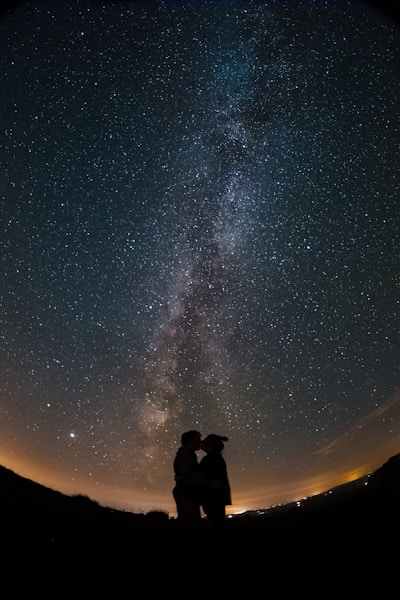 silhouette of 2 person standing under starry night