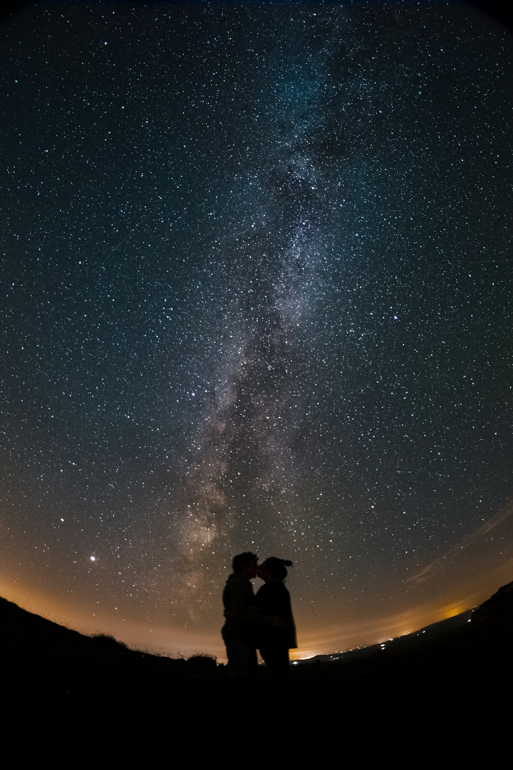Silhouette von 2 Personen, die unter Sternennacht stehen
