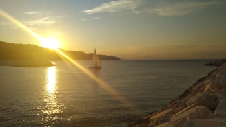 A serene Tunisian coastline with a sailboat gliding over calm blue waters at sunset.