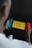 A person is holding a portable gaming console displaying the title screen for a game called 'Pokémon Quest.' The console has blue and red controllers attached to it, and the words 'Tap to start' are visible on the screen against a yellow background.