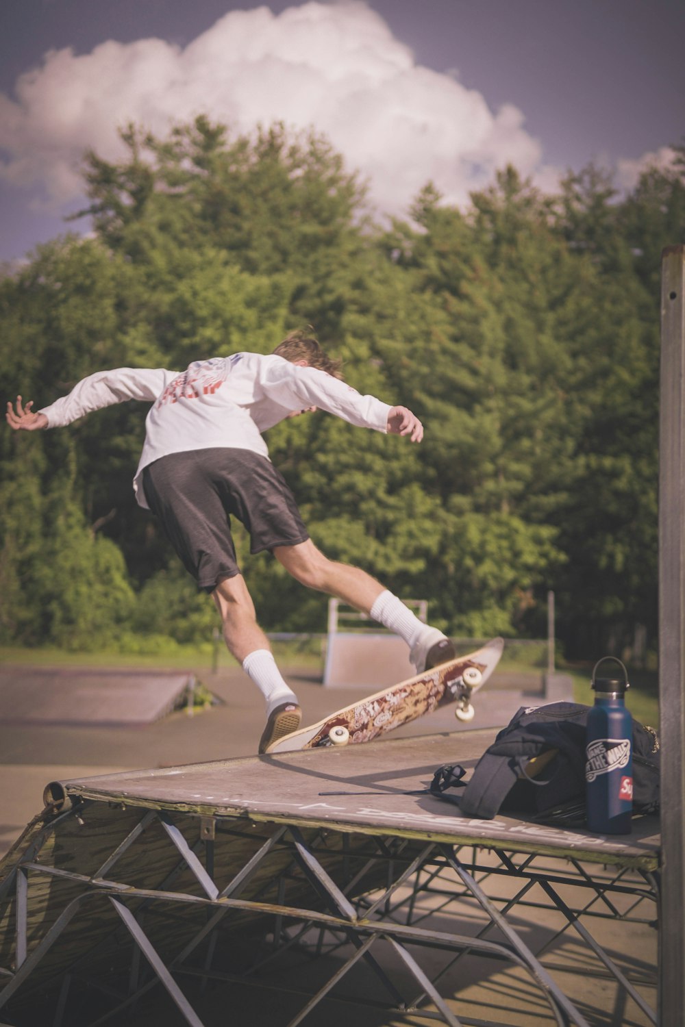 man in white long sleeve shirt and black pants jumping on brown skateboard during daytime