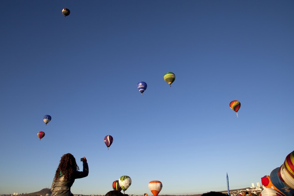 man in black jacket standing on the field with hot air balloons