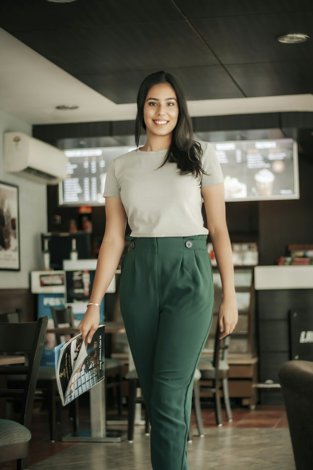 woman in white shirt and green pants standing near black chair