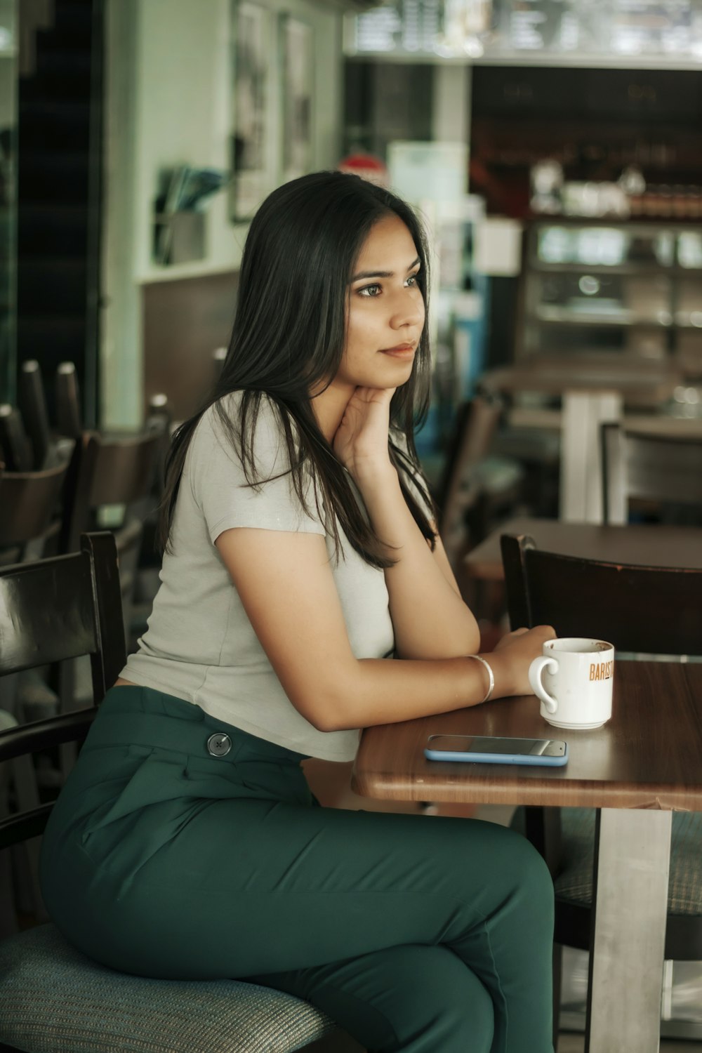 woman in white t-shirt and green skirt sitting on chair holding white ceramic mug