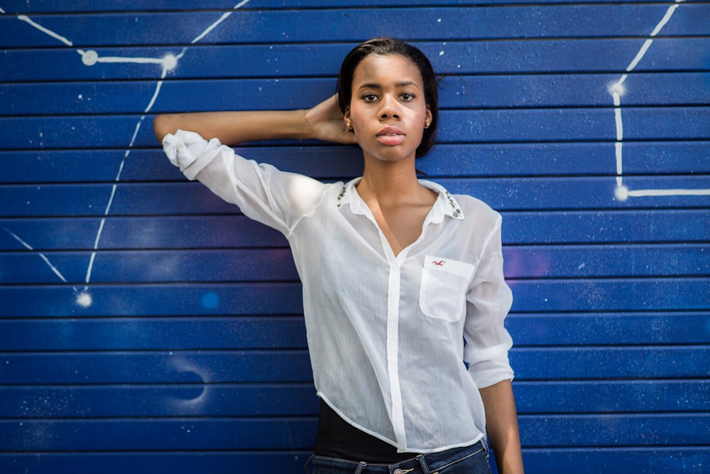 woman in white dress shirt and black pants standing beside blue wall
