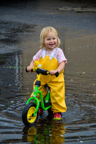 A cheerful toddler confidently riding an orange tinywheelz balance bike on a sunny park path.