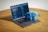 A laptop displaying code on its screen sits on a wooden table, with a blue plush toy elephant branded with 'PHP' perched on its keyboard.