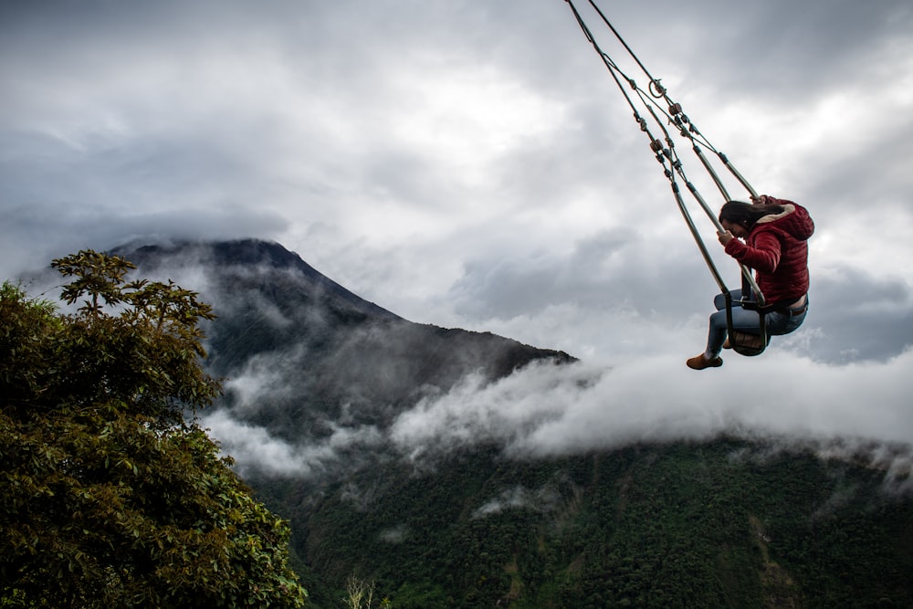 man in blue jacket and black pants riding on cable car over green mountain during daytime