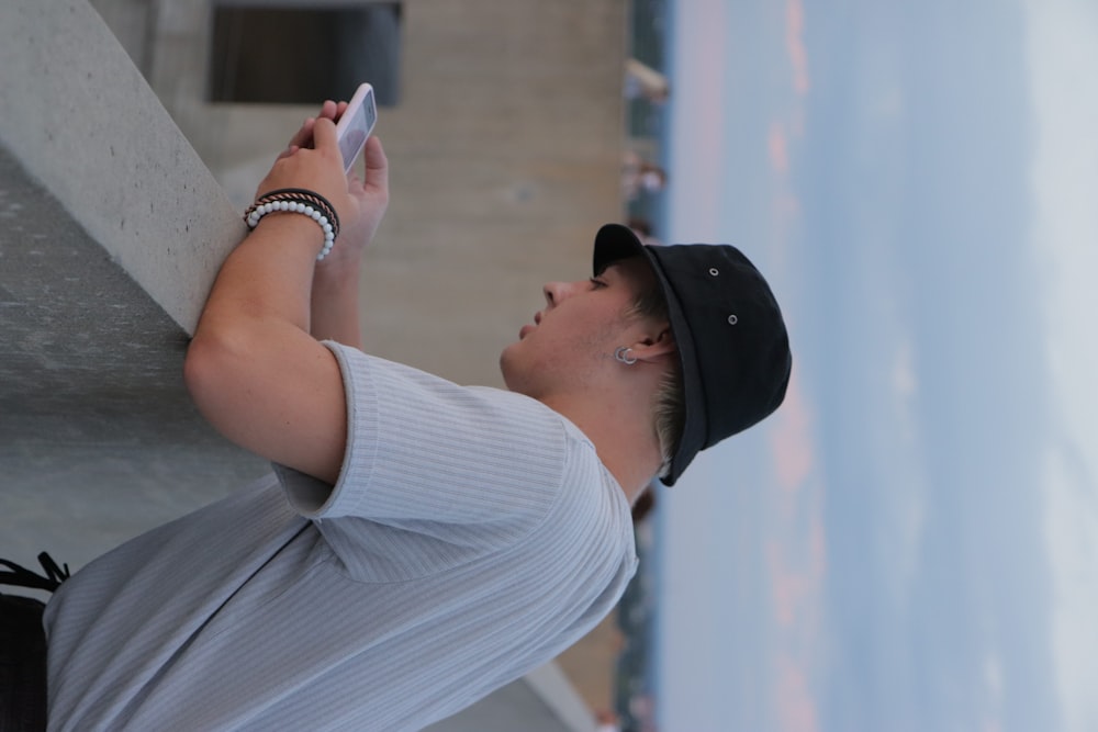 man in white crew neck t-shirt and black cap holding smartphone