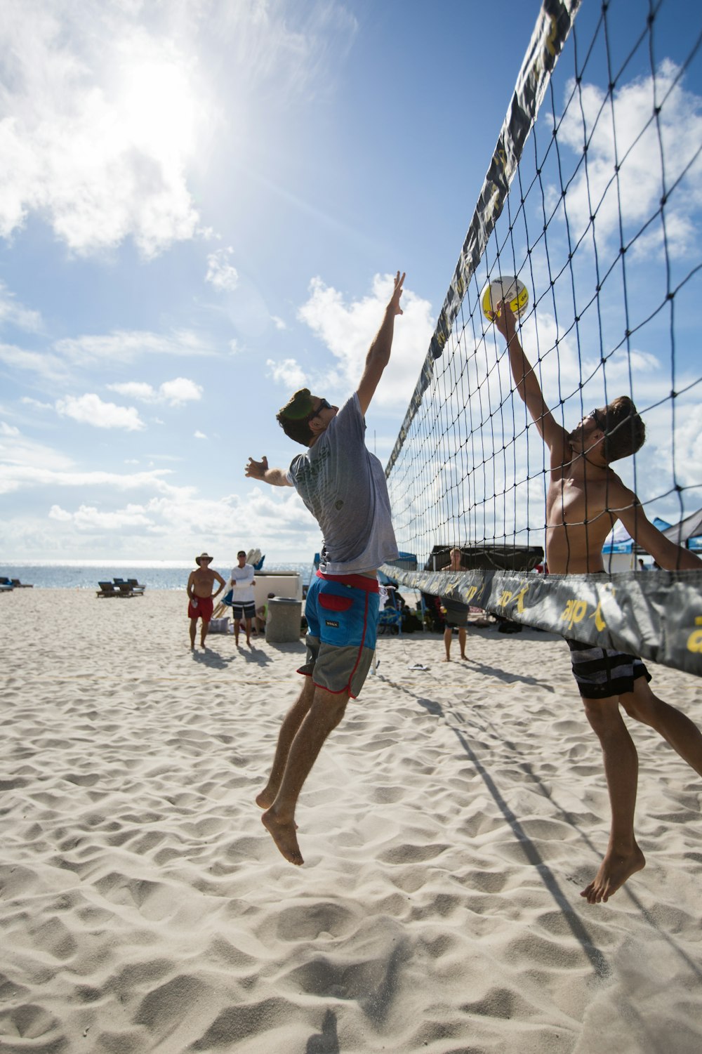 hombre con camisa blanca y pantalones cortos azules jugando voleibol en la playa durante el día