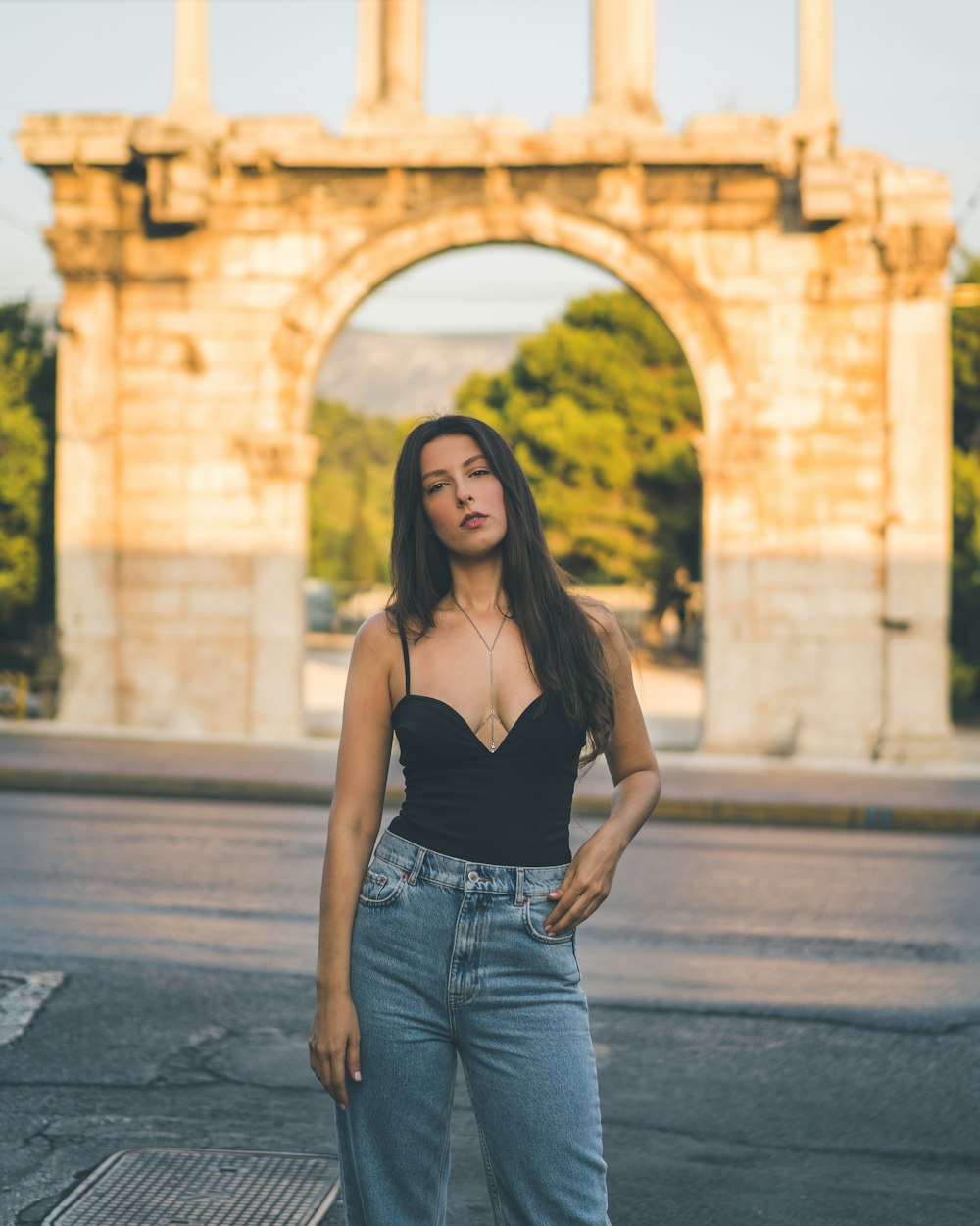 woman in black spaghetti strap top and blue denim jeans standing on sidewalk during daytime