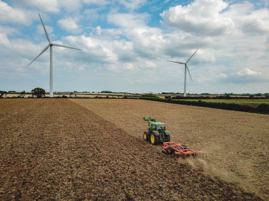 green and red tractor on brown field under blue and white cloudy sky during daytime