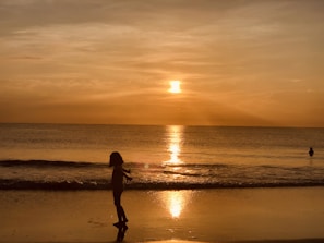 A sunset silhouette of a child running on the beach with a Marea poncho fluttering