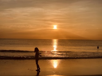 A sunset silhouette of a child running on the beach with a Marea poncho fluttering