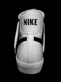 A close-up view of the back of a white high-top sneaker with the brand name printed in bold letters. The shoe features white laces, detailed stitching, and a textured sole. The background is a solid black, highlighting the sneaker.