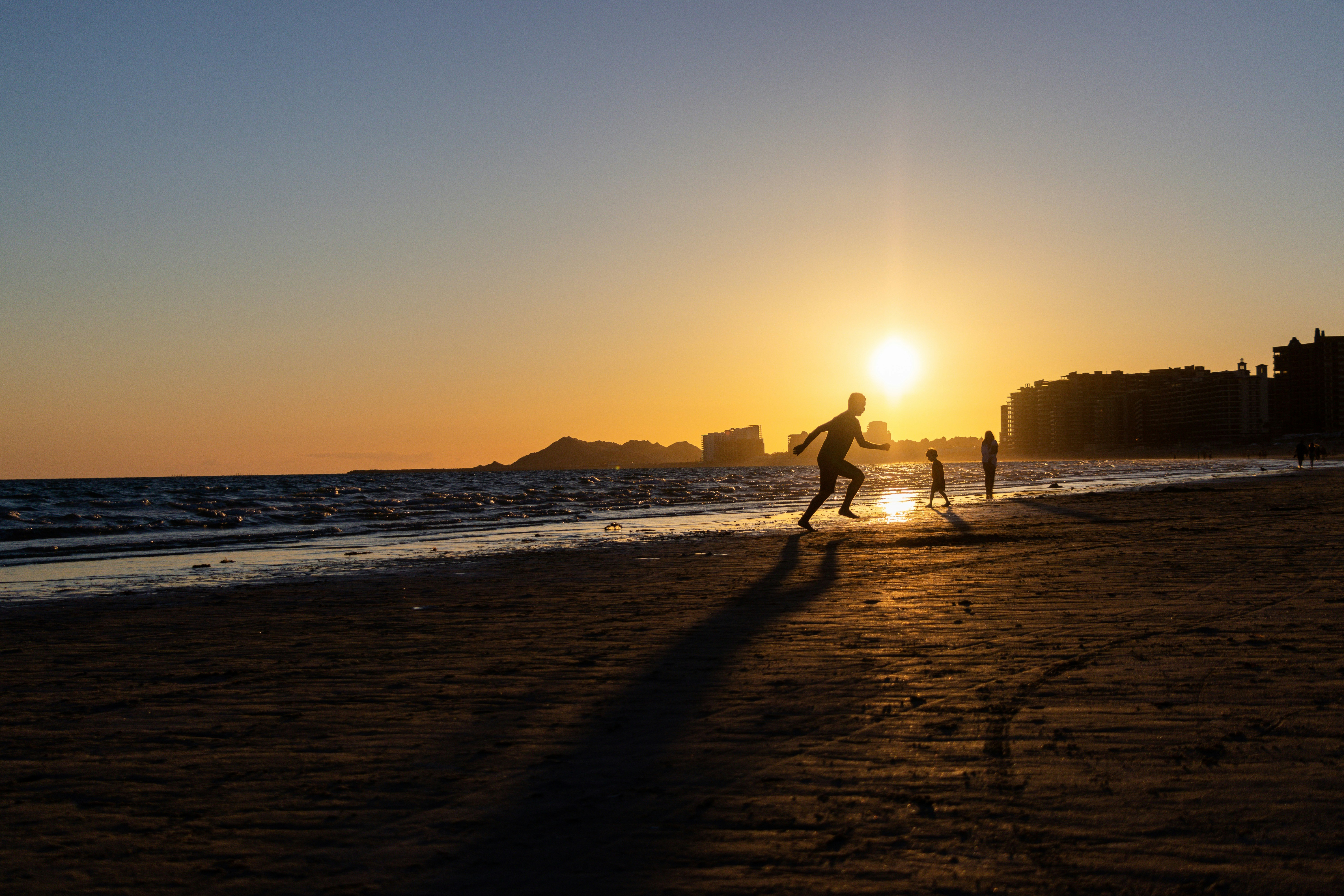 silhouette of man and woman walking on beach during sunset