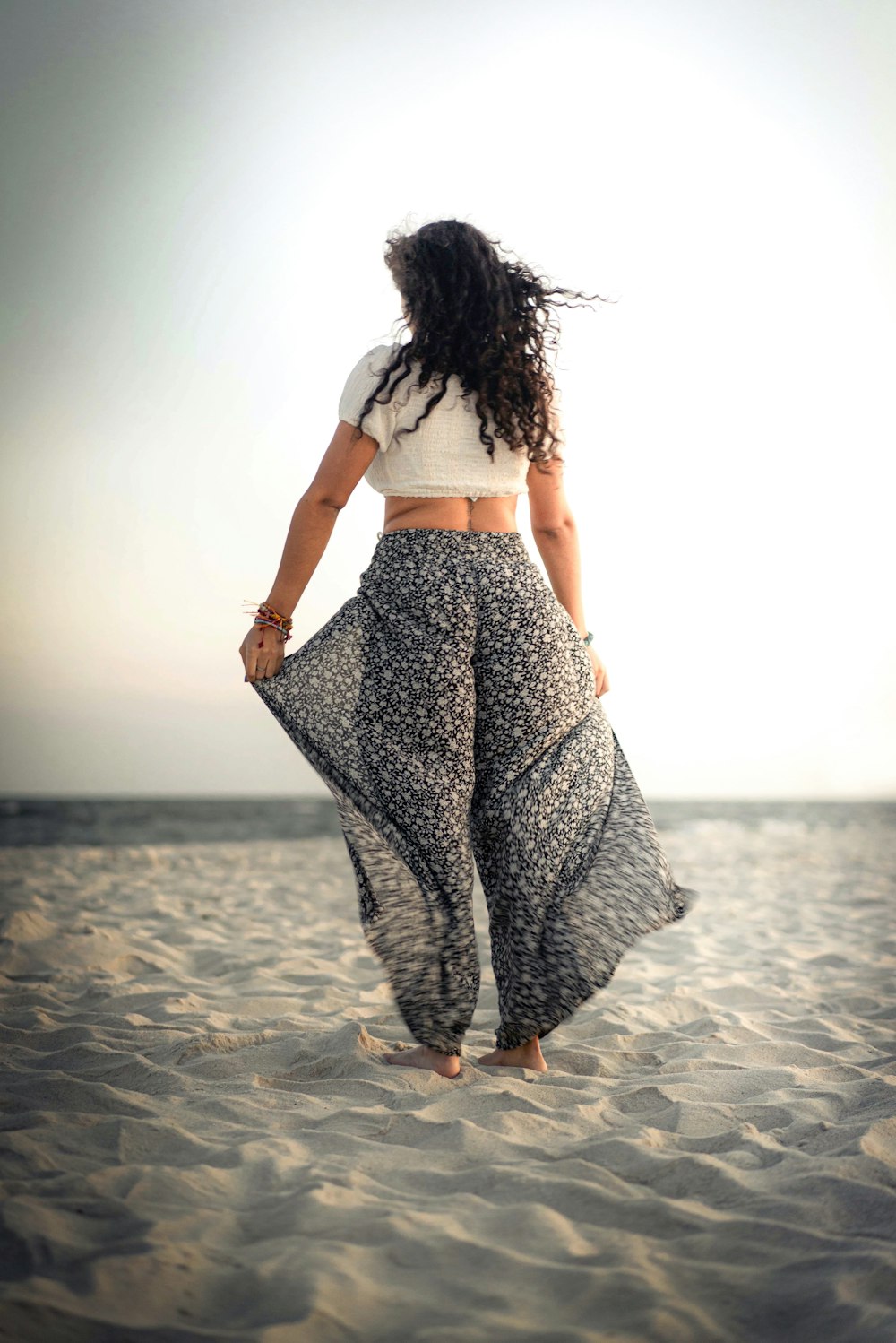 woman in white shirt and black and white skirt walking on beach during daytime