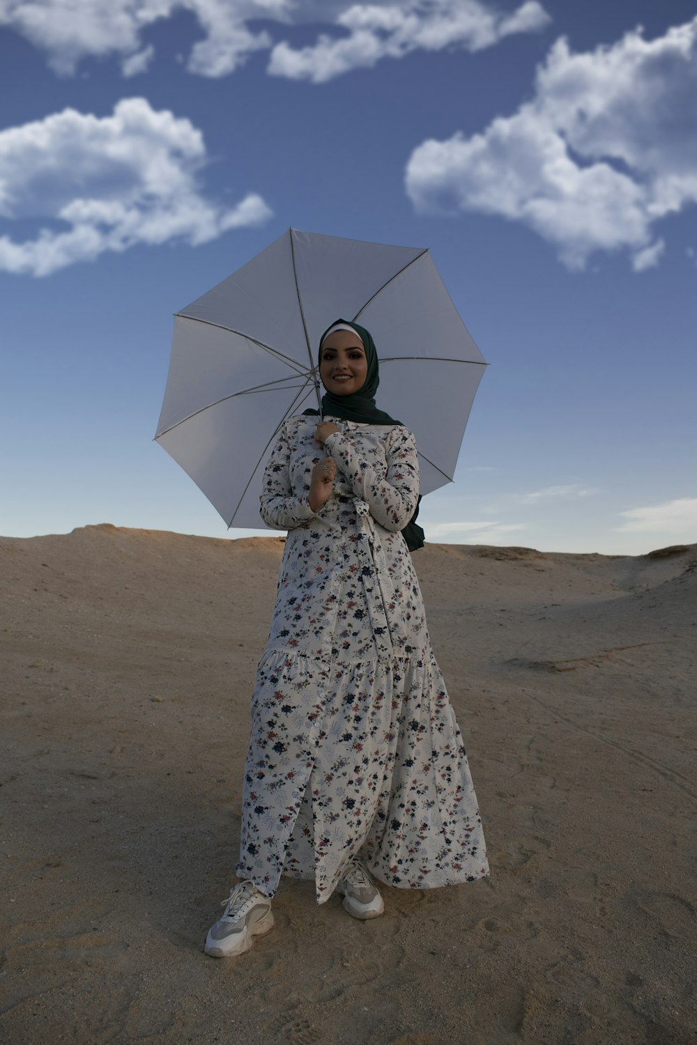 woman in white and black floral dress holding umbrella walking on brown sand during daytime