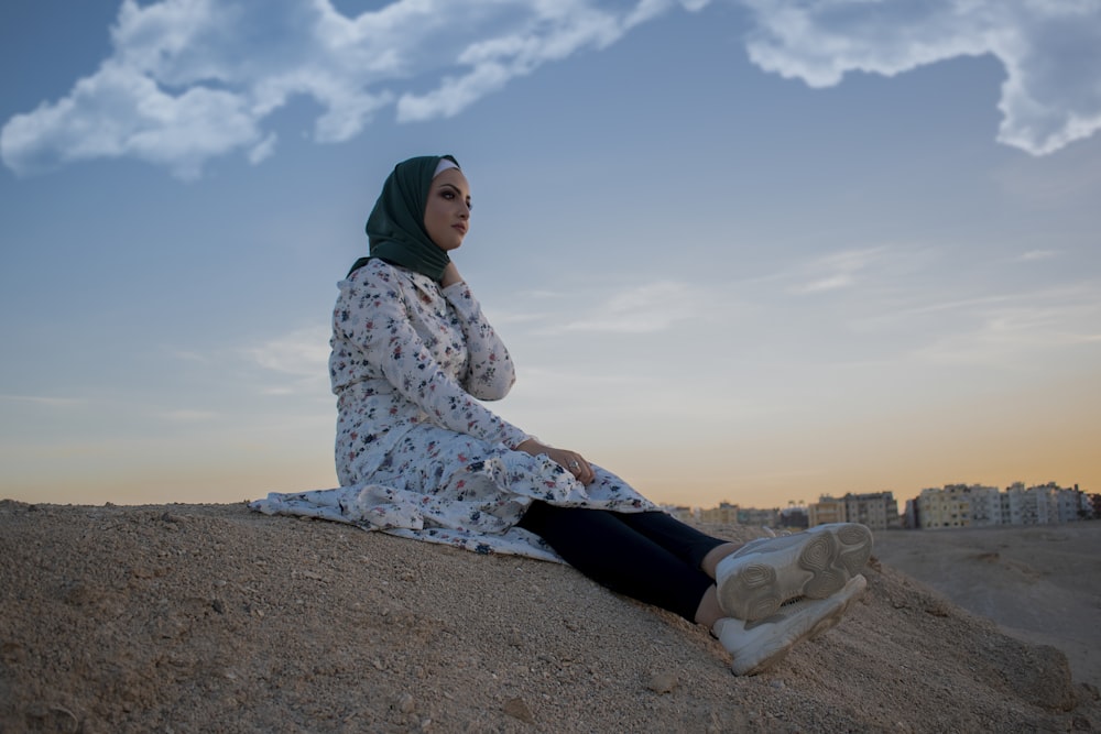 woman in white and blue floral hijab sitting on brown sand during daytime