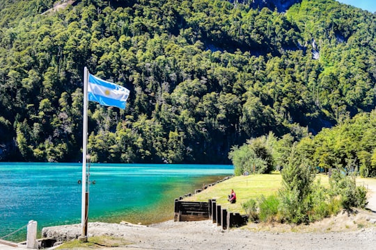 blue flag on brown wooden bench near body of water during daytime in Puerto Blest Argentina