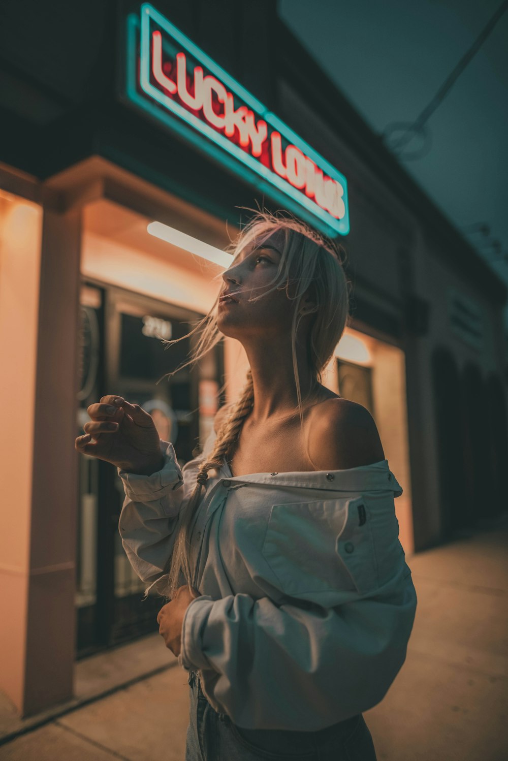 woman in white off shoulder dress standing near red and white open neon signage