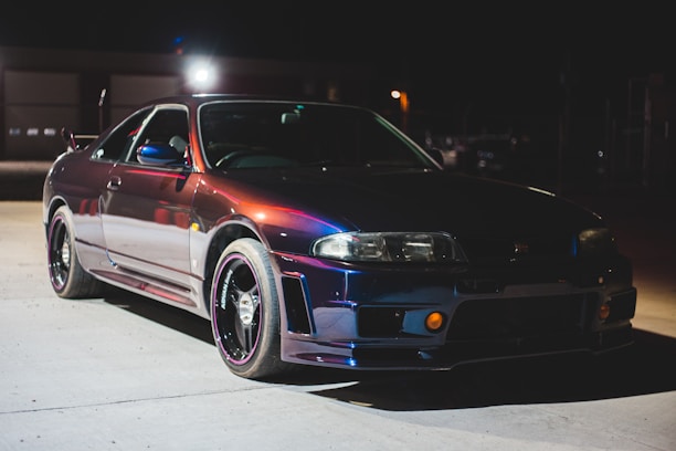 A sleek black sports car parked under moody dark blue lighting, highlighting its curves.