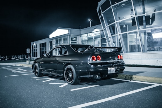 A sleek black sports car parked beside a modern glass-walled gym at sunset.