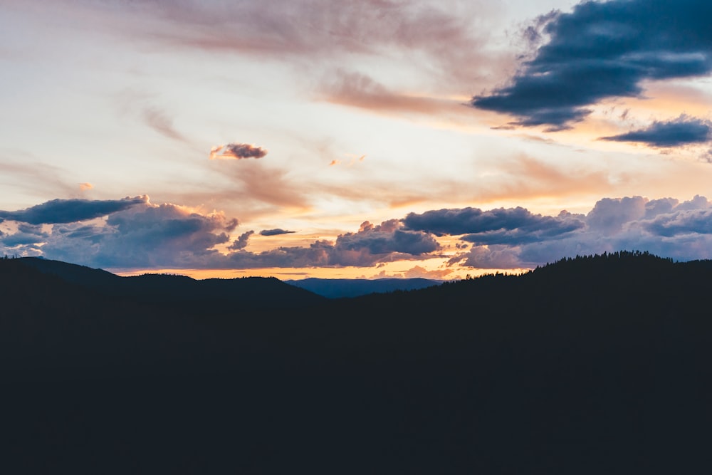 silhouette of mountain under cloudy sky during sunset