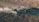 Aerial view of a combine harvester operating in a vast field, collecting crops. A tractor with an attached trailer follows behind, filled with harvested produce. Dust trails form in the wake of the machinery, creating a dynamic scene illustrating agricultural work.