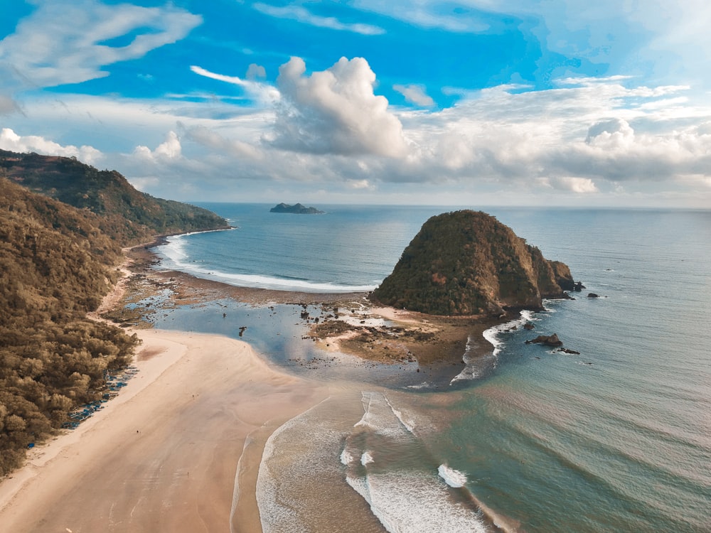 brown rock formation on sea shore under blue and white sunny cloudy sky during daytime