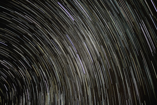 Long exposure photograph capturing the circular trails of stars across the night sky, creating graceful arcs of light.