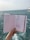 A hand holds a sketchbook open to reveal fashion illustrations against a background of the sea. The sketches depict clothing designs, including a long dress and a jumpsuit, both enhanced with detailed patterns. The ocean is visible in the distance, with slight waves under a muted sky.