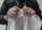 Hands are gripping a sheet of bubble wrap, with a person wearing a black shirt and a lanyard visible. A ring is worn on the left hand, and the bubble wrap is being pulled taut, suggesting potential for popping.