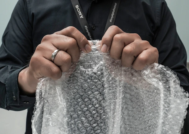 Close-up of hands securing fragile items with bubble wrap and tape before packing.