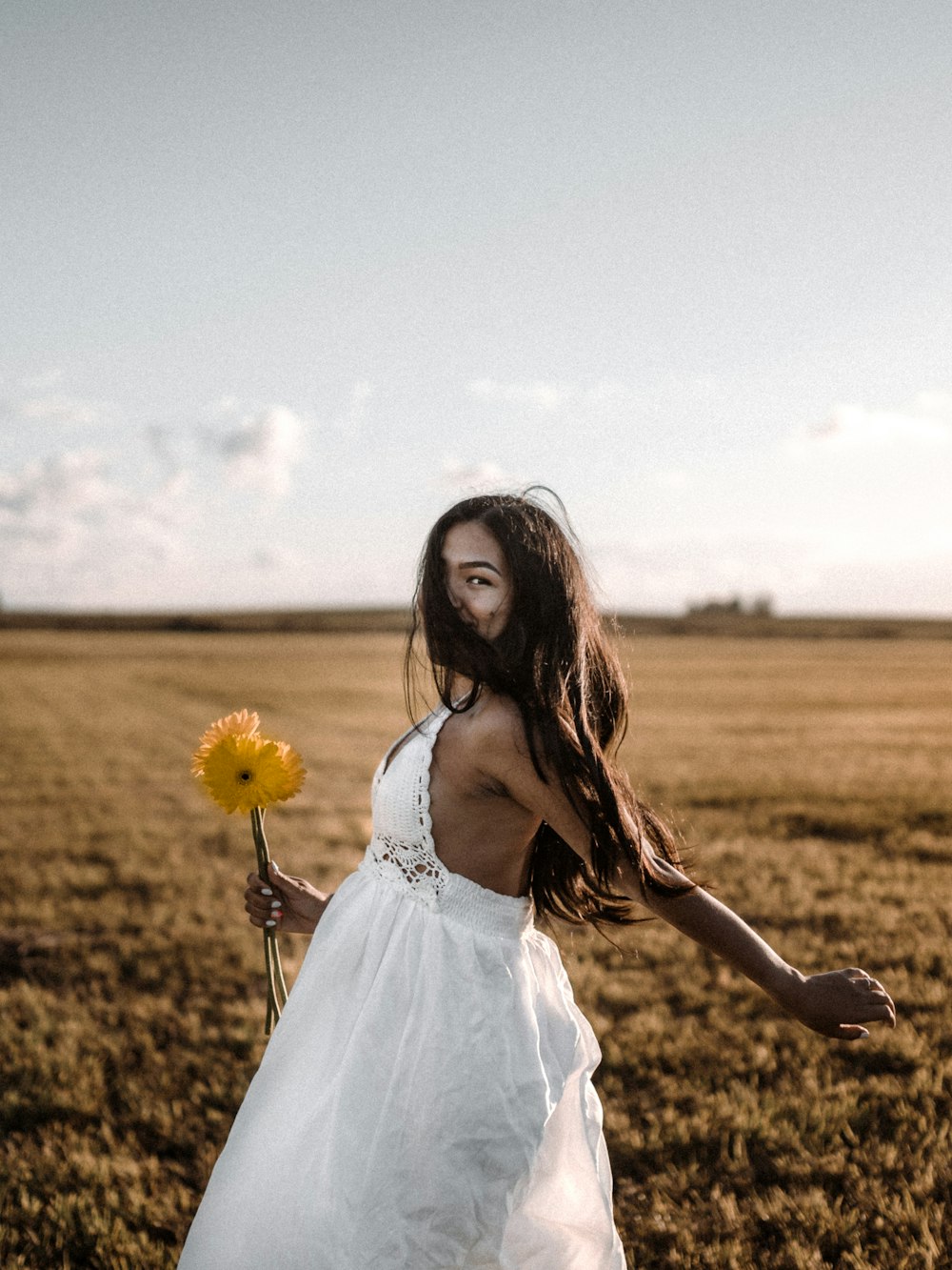 femme en robe blanche debout sur le champ d’herbe brune pendant la journée
