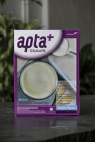 A box featuring a health-related product labeled 'apta+ Glukofit' with a purple and white design. The product claims a vanilla flavor and highlights benefits for diabetes, including low sodium and lactose content, high fiber, vitamins, and calcium. The front design includes a photo of a white beverage to suggest consumption.