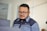 A man with glasses is focused on his work in a modern office setting, wearing a dark uniform. The background is softly blurred, emphasizing the clean and professional environment.
