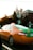A green and orange taxi with a visible phone number on its sign is parked on a street in front of residential houses. The surrounding area includes trees and a typical suburban neighborhood environment.