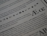 The image displays a close-up of printed text on a page. Various typographic symbols and special characters are highlighted, including a scissors icon, a hand pointing, and different shapes and icons such as arrows, hearts, and musical notes. The text is related to typography and typefaces, discussing characters and ligatures like Æ and œ.