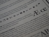 The image displays a close-up of printed text on a page. Various typographic symbols and special characters are highlighted, including a scissors icon, a hand pointing, and different shapes and icons such as arrows, hearts, and musical notes. The text is related to typography and typefaces, discussing characters and ligatures like Æ and œ.