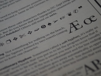 The image displays a close-up of printed text on a page. Various typographic symbols and special characters are highlighted, including a scissors icon, a hand pointing, and different shapes and icons such as arrows, hearts, and musical notes. The text is related to typography and typefaces, discussing characters and ligatures like Æ and œ.